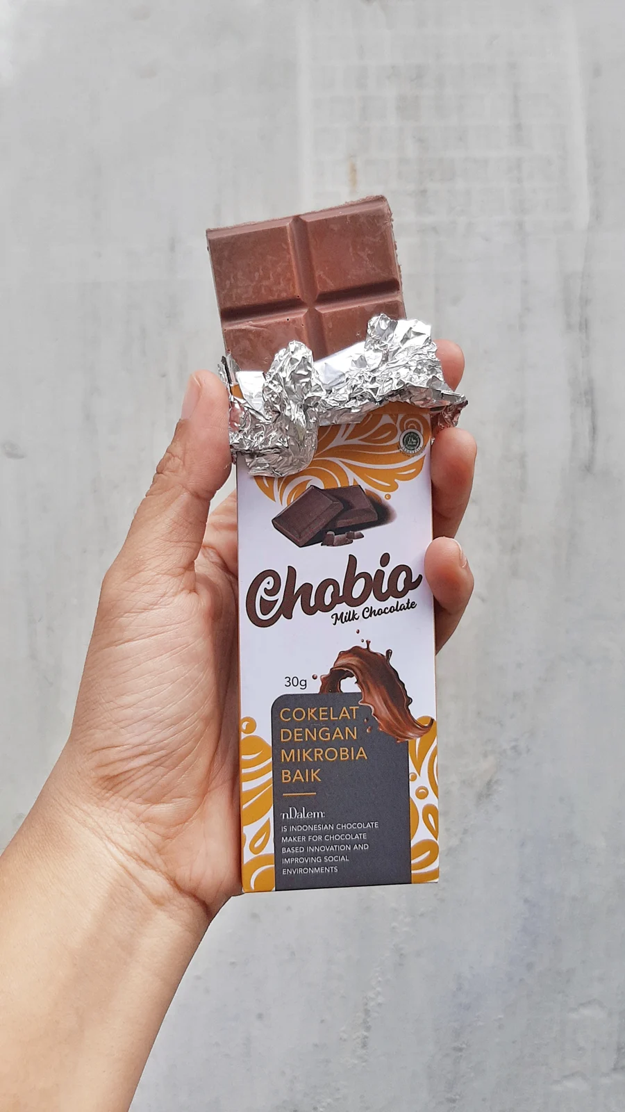 Tangan memegang Chobio yang sudah dibuka, memperlihatkan cokelat susu dan pembungkus foil